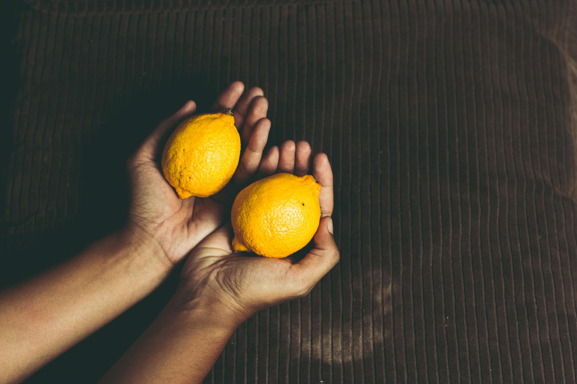 Two fresh lemons cupped in hands on a brown surface, symbolizing gentle restoration.