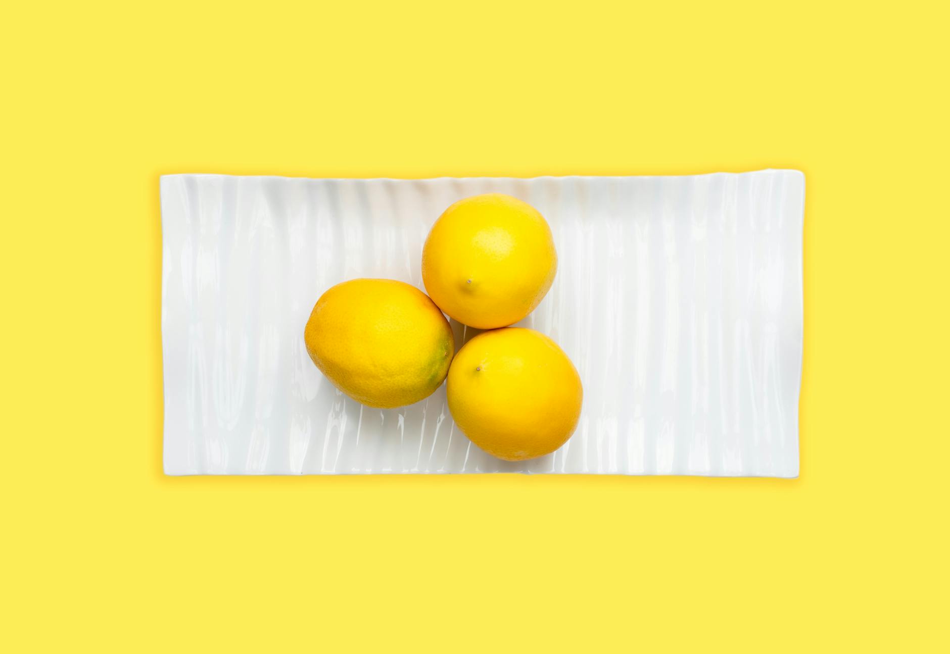 Hand holding a fresh lemon against a bright yellow background, symbolizing the refreshing sensation of renewed pleasure.