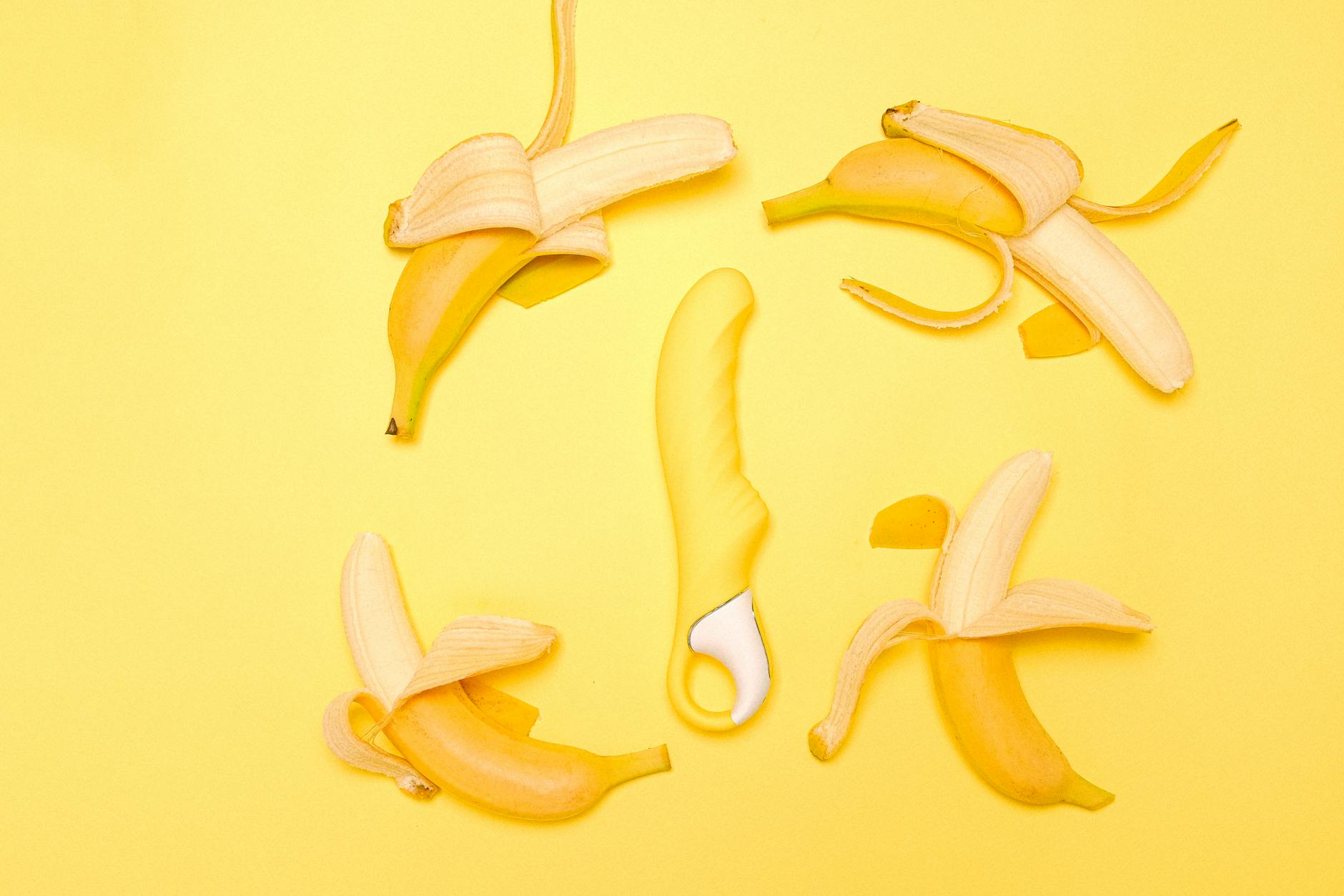 Yellow silicone vibrator surrounded by peeled lemons on a bright yellow background