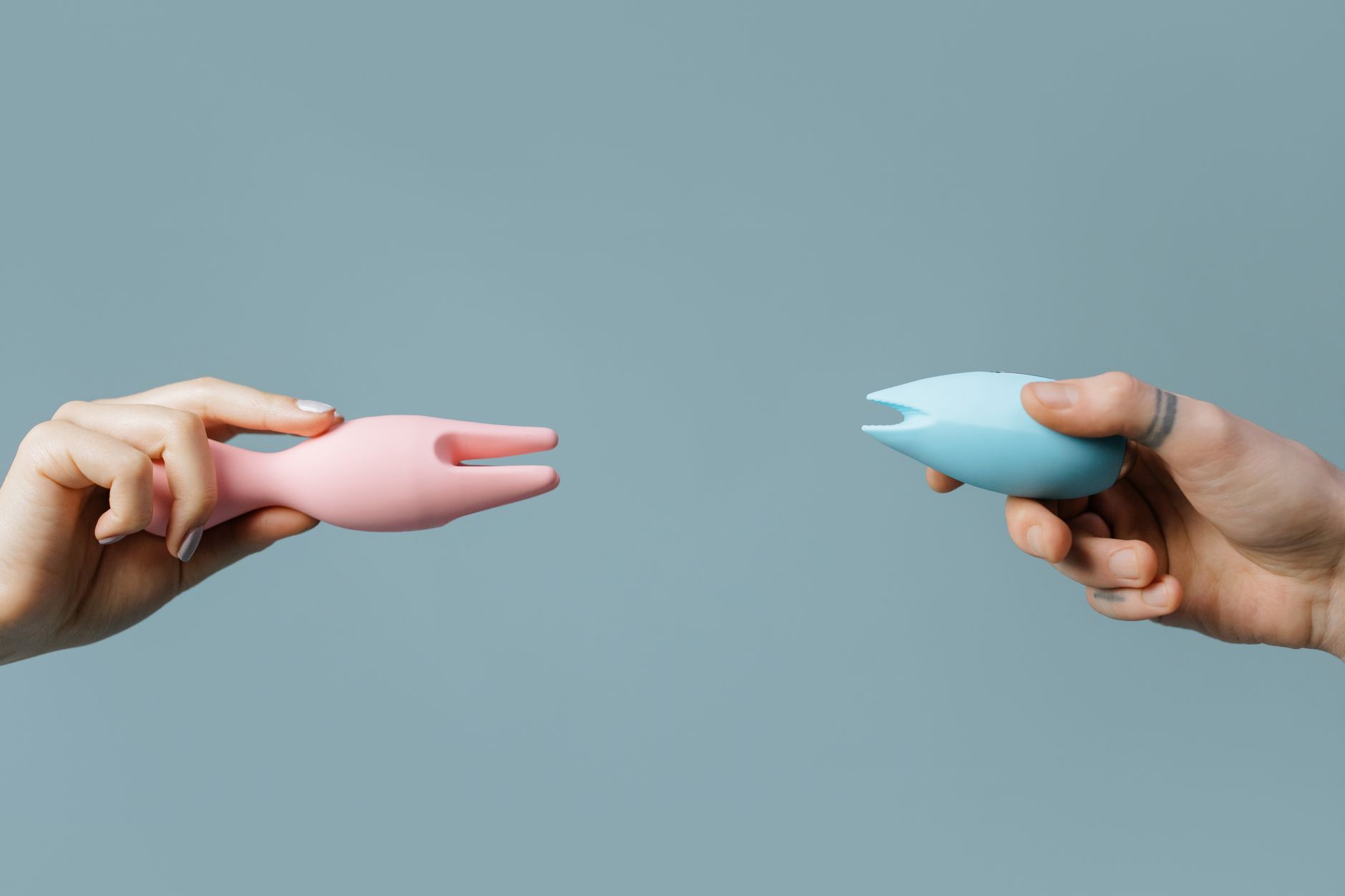 Two hands holding vibrators against a pastel background, representing intimate wellness tools