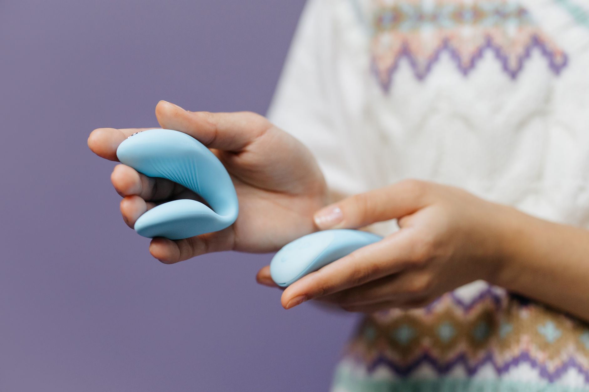 Mano sosteniendo un vibrador azul moderno contra fondo púrpura
