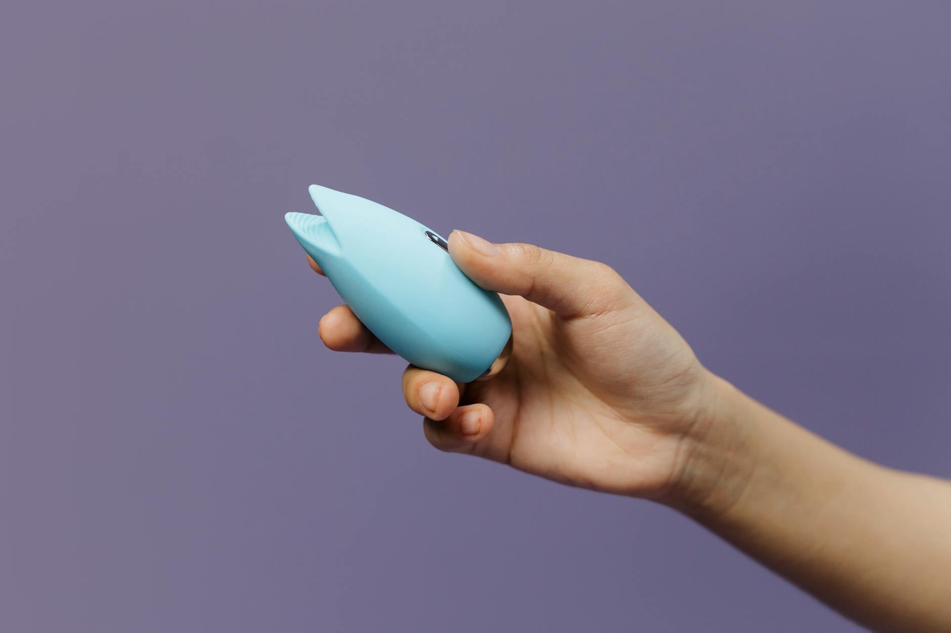 A blue lemon clitoral vibrator held in hand against a solid purple background, promoting self-awareness and reconnection to pleasure
