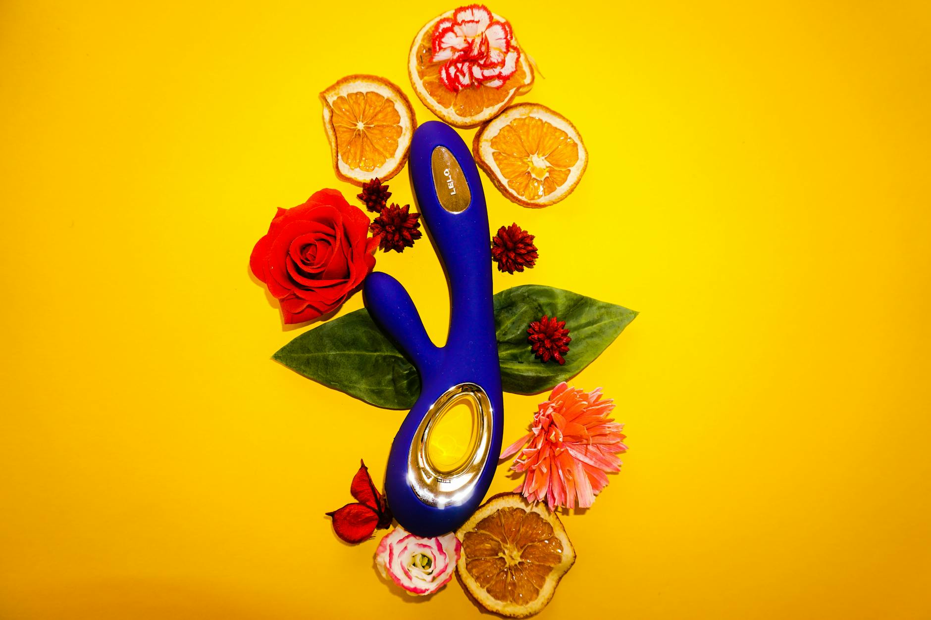 A blue lemon vibrator surrounded by fresh lemons and flowers on a bright yellow background.