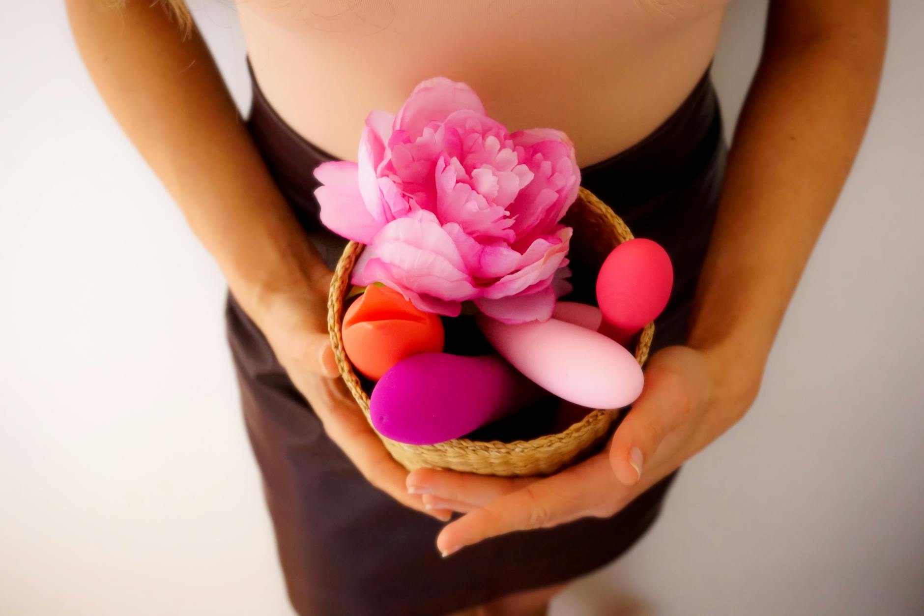 A basket of colorful clitoral vibrators and flowers on a soft surface, representing pleasure tools for different bodies.